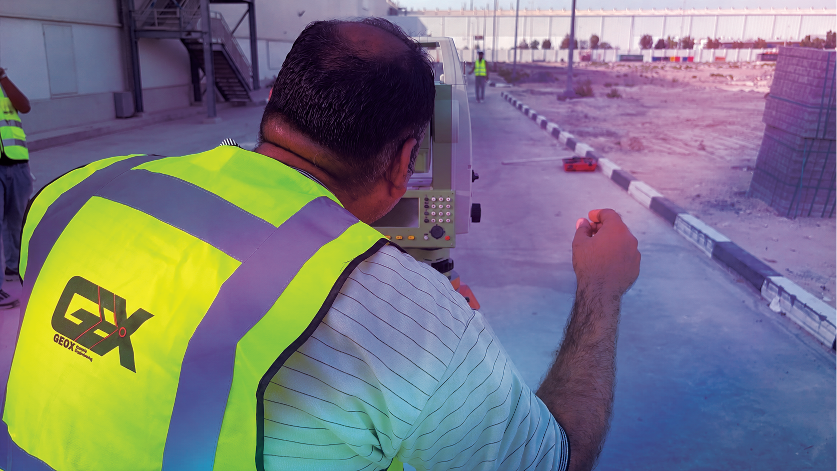 GeoX surveyor operating a total station beside a construction site access road.