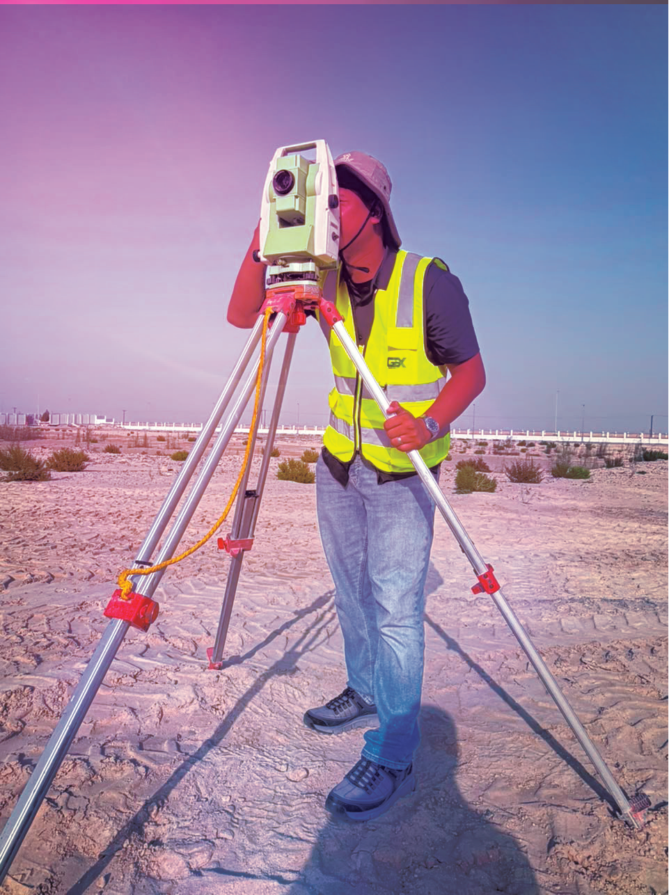 GeoX surveyor looking through a total station on a tripod at an outdoor site.