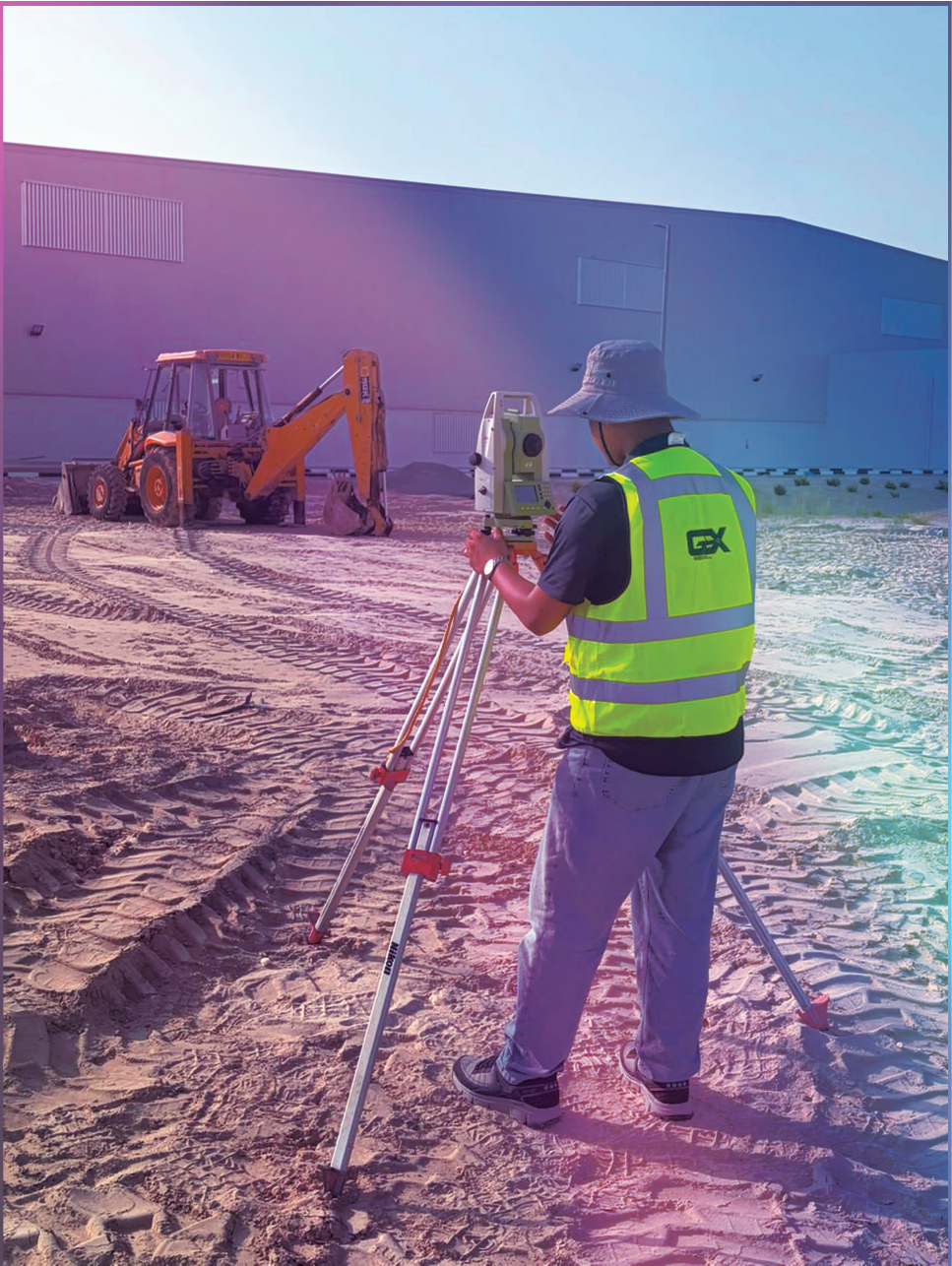 GeoX surveyor setting up a total station beside an excavator and industrial building.